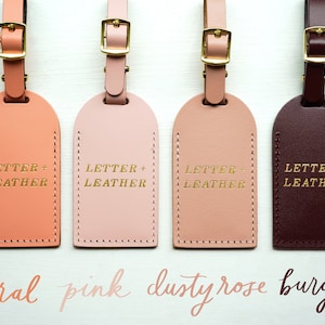 K&ouml;nnte beinhalten: Vier Leder-Gep&auml;ckanh&auml;nger in den Farben Koralle, Rosa, Altrosa und Burgunderrot. Jeder Anh&auml;nger hat eine goldene Beschriftung mit dem Text "LETTER + LEATHER".