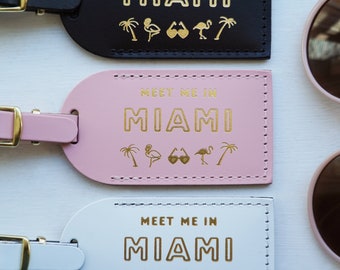 May include: Three luggage tags with gold lettering that reads "Meet me in Miami" with palm trees, flamingos, and sunglasses. The tags are black, pink, and white.