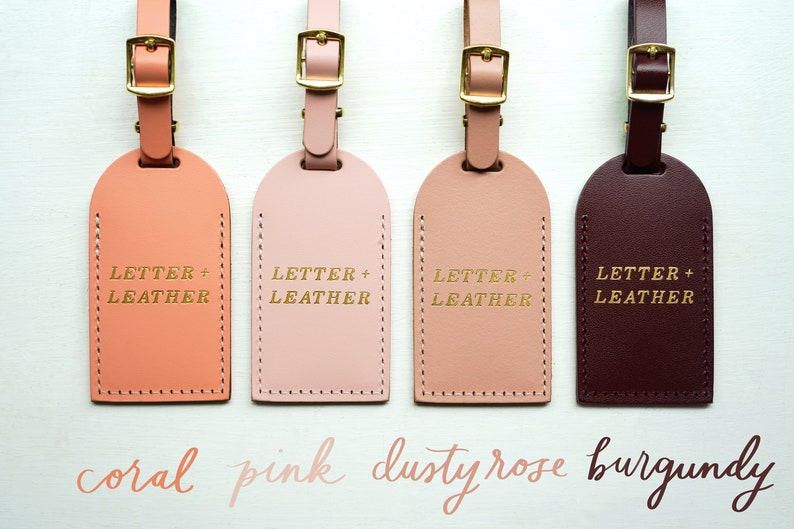 May include: Four leather luggage tags in coral, pink, dusty rose, and burgundy colors. Each tag has gold lettering that reads "LETTER + LEATHER".