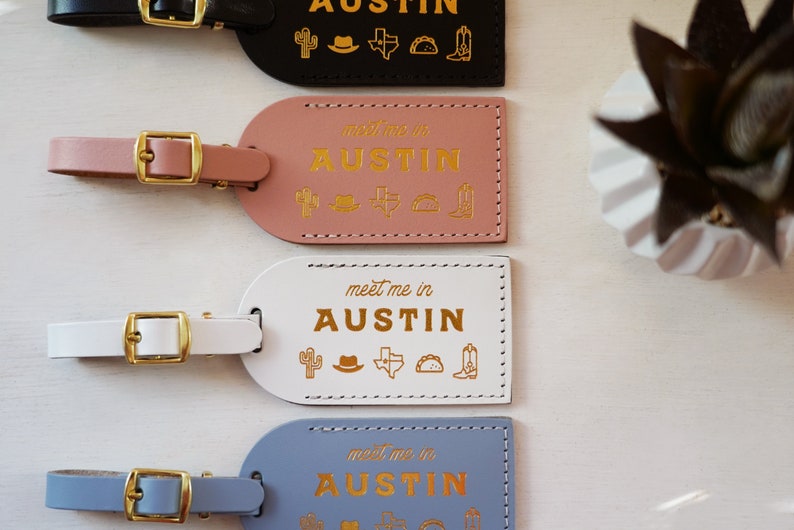 K&ouml;nnte beinhalten: Vier Leder-Gep&auml;ckanh&auml;nger mit goldener Beschriftung "meet me in AUSTIN" und einem Kaktus, einem Cowboyhut, einem Texas-Stern, einem Taco und einem Cowboystiefel. Die Anh&auml;nger sind in Schwarz, Rosa, Wei&szlig; und Blau.