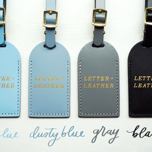 May include: Four leather luggage tags in sky blue, dusty blue, gray, and black with gold lettering that reads "LETTER + LEATHER".