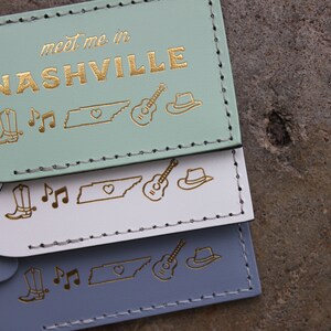 May include: Three luggage tags with the text "meet me in NASHVILLE" in gold lettering. The tags are in mint green, white, and light blue. Each tag features a gold outline of a cowboy boot, musical notes, the state of Tennessee, a guitar, and a cowboy hat.