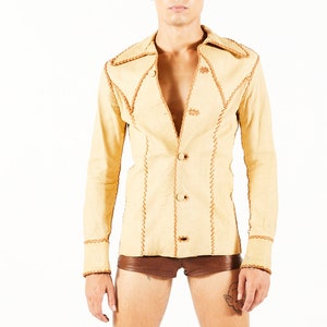 Puede incluir: Chaqueta color beige con costuras y botones marrones, pantalones cortos marrones y botas de plataforma negras. Las botas tienen rayas coloridas y una suela estampada. La persona está de pie frente a un fondo blanco.