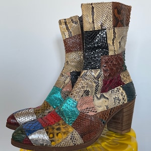 May include: A pair of colorful patchwork heeled boots made from different types of snakeskin. The boots have a chunky heel and a zipper on the inside of the ankle.