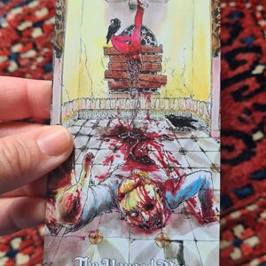 May include: A tarot card illustration depicting a figure hanging upside down, with blood and crows. The card is titled "The Hanged Man". The artwork features a detailed, macabre scene with a vintage aesthetic.