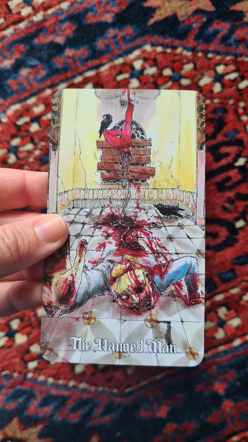 May include: A tarot card illustration depicting a figure hanging upside down, with blood and crows. The card is titled "The Hanged Man". The artwork features a detailed, macabre scene with a vintage aesthetic.