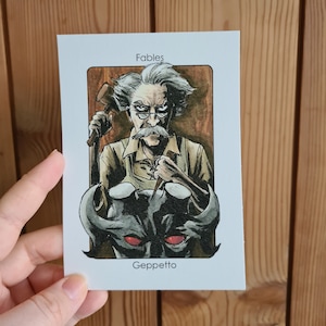 May include: A card from the Fables series featuring a black and white illustration of Geppetto, a character from the story of Pinocchio. Geppetto is depicted as an older man with a white beard and mustache, wearing a brown shirt and overalls. He is holding a wooden puppet in his hands. The card has the title "Fables" at the top and "Geppetto" at the bottom.