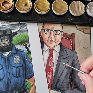 May include: A watercolour painting of a man in a suit and tie. He is sitting in a chair with a cross on his lapel. The painting is being worked on with a paintbrush.