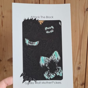 May include: A black and white illustration of a monster with sharp teeth and the text "Attack The Block" and "Gorilla Wolf Motherf*ckers".