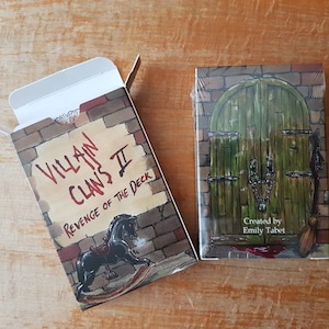 May include: A box for a deck of playing cards called "Villain Clans II: Revenge of the Deck". The box is red, white, and black with a brick pattern and a rocking horse illustration. The text "Created by Emily Tabet" is on the front of the box.