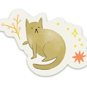 Op de afbeelding: Een grillige sticker met een illustratie van een bruine kat met een ietwat humeurige uitdrukking. De kat is omringd door decoratieve elementen, waaronder een takje met roze bessen, gele sterren en een oranje ster. De sticker heeft een witte rand.
