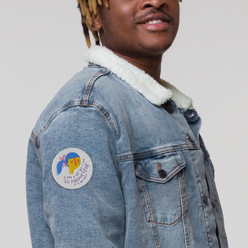 K&ouml;nnte beinhalten: Eine blaue Jeansjacke mit einem wei&szlig;en Sherpa-Kragen. Die Jacke hat einen Aufn&auml;her auf der linken Seite, auf dem steht "Ich weine viel, aber ich bin so produktiv, dass es nicht mal lustig ist".