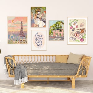 May include: Five framed prints on a white wall above a gray couch with a wicker frame. The prints feature illustrations of Paris, including the Eiffel Tower, a cafe, a pink building, and a croissant with coffee.