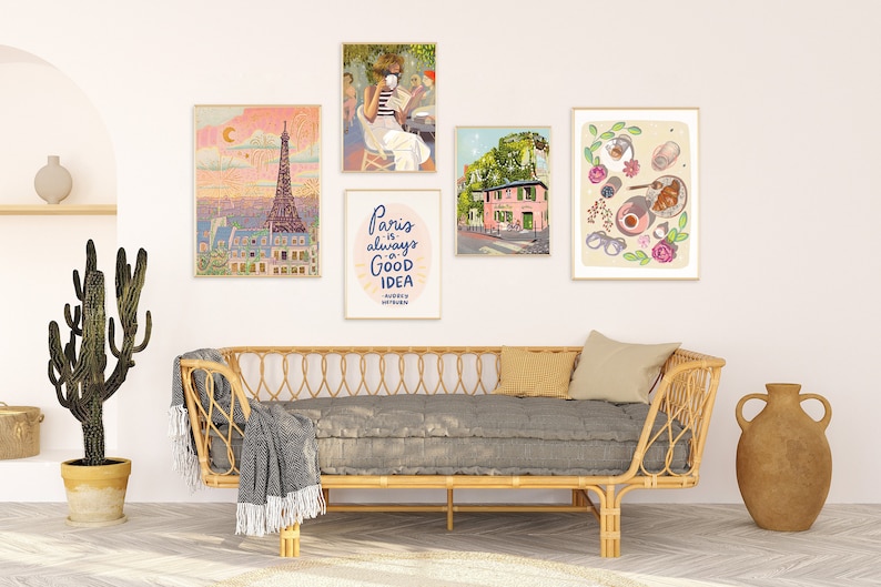 May include: Five framed prints on a white wall above a gray couch with a wicker frame. The prints feature illustrations of Paris, including the Eiffel Tower, a cafe, a pink building, and a croissant with coffee.