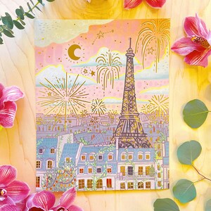 K&ouml;nnte beinhalten: Eine farbenfrohe Illustration des Eiffelturms in Paris, Frankreich, mit Feuerwerk, das in den Himmel explodiert. Die Illustration ist vor einem rosa und blauen Sonnenuntergang mit Sternen und einer Mondsichel platziert. Der Eiffelturm ist von Geb&auml;uden und B&auml;umen umgeben.