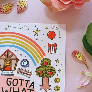 Może przedstawiać: Kapryśna ilustracja z tęczą, domem, jabłonią i napisem "GOTTA WHAT". Czerwony balon jest przymocowany do pudełka z prezentem. Gwiazdy i monety są rozrzucone na r&oacute;żowym tle.