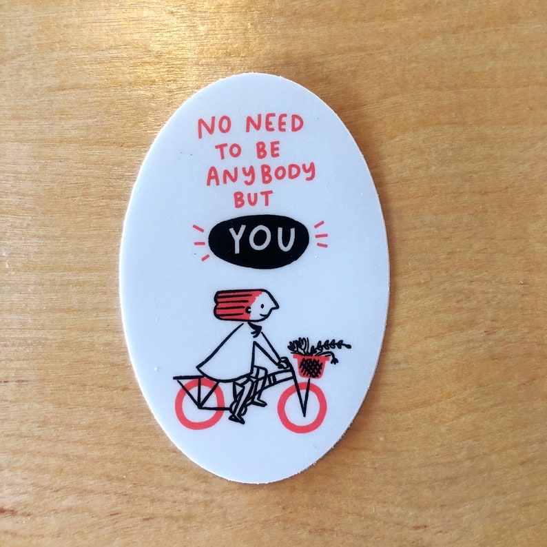 May include: White oval sticker with a black and white illustration of a person riding a bicycle with a basket of flowers. The text on the sticker reads "No need to be anybody but you".