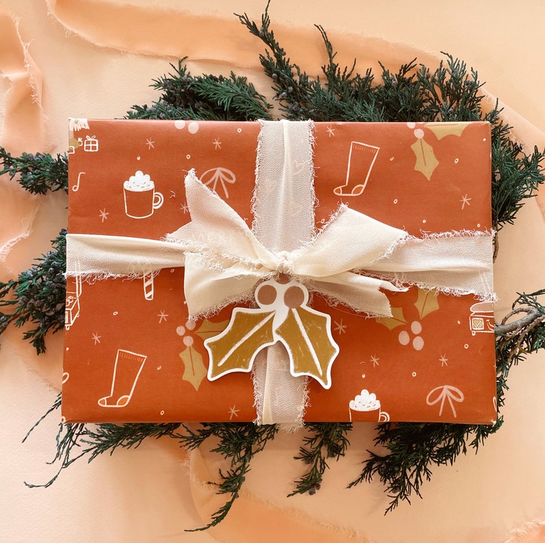May include: A brown gift box with a white ribbon and a holly leaf design. The box is wrapped in festive paper with a pattern of stars, snowflakes, and other wintery motifs.