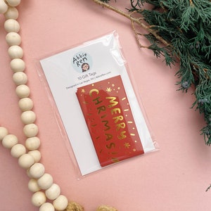 May include: A pack of 10 red gift tags with gold foil lettering that says "Merry Christmas!" Designed by Abbie Ren.