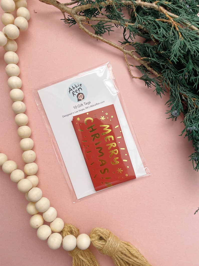 May include: A pack of 10 red gift tags with gold foil lettering that says "Merry Christmas!" Designed by Abbie Ren.