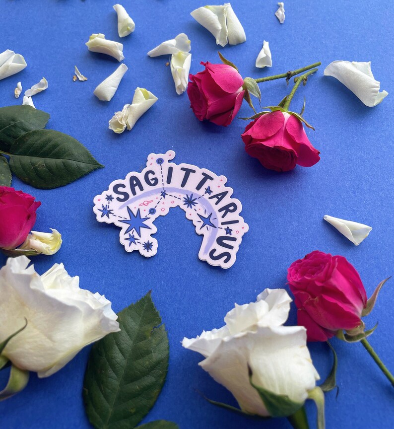 May include: A white sticker with a blue constellation design and the text "SAGITTARIUS" on a blue background with white and pink roses.