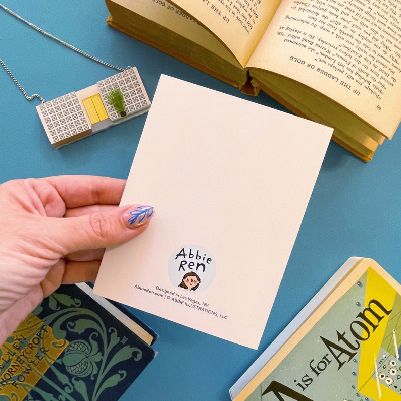 May include: A white card with a blue and white illustration of a person with the text "Abbie Ren" in a circle. The text "Designed in Las Vegas, NV" and "AbbieRen.com &copy; ABBIE ILLUSTRATIONS, LLC" are also on the card.