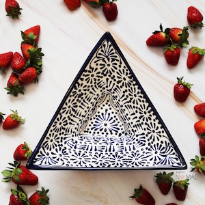 May include: Triangular ceramic serving dish with a blue and white floral pattern. The dish has a dark blue border and is surrounded by fresh strawberries. The dish is approximately 30 cm wide.