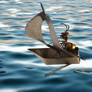 May include: A rusty metal sculpture of an ant sailing a boat on a blue and white water background.