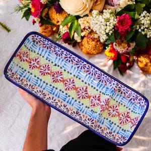May include: A colorful ceramic serving dish with a blue rim and a geometric pattern in shades of red, yellow, blue, and green. The dish has three sections.