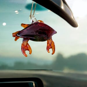 May include: A purple glass crab ornament with orange claws hanging from a rearview mirror in a car.