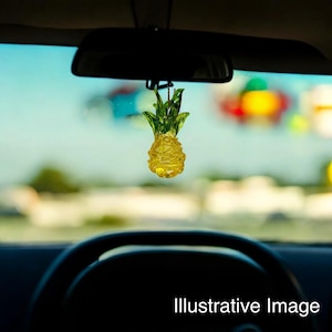 May include: A yellow and green pineapple-shaped car air freshener hanging from the rearview mirror of a car.