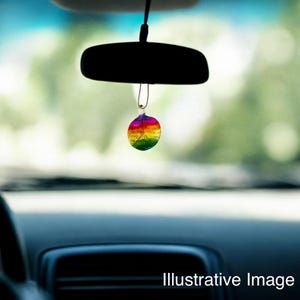 May include: A rainbow-colored glass ornament hanging from the rearview mirror of a car. The ornament is round and has a peace sign design.