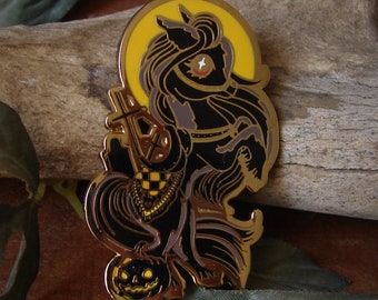 May include: A black and gold enamel pin featuring a black horse with a crescent moon behind it. The horse is holding a cross and has a pumpkin at its feet.