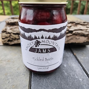 May include: A glass jar with a gold lid filled with pickled beets. The jar has a white label with black text that reads "Smoky Mountain Jams Pickled Beets 1 pint (473 ml)".