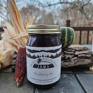May include: A glass jar of Smoky Mountain Jams Blackberry Jam. The jar has a gold lid and a white label with black text. The label reads "Smoky Mountain Jams Blackberry Jam 1 pint (1 lb. 3 oz.) 538 grams".