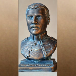 Puede incluir: Un busto de bronce de Freddie Mercury, el cantante principal de Queen, con un rostro esculpido detallado y un busto texturizado y en capas. El busto está sobre una base rectangular con las palabras "Freddie Mercury" inscritas en la parte delantera.