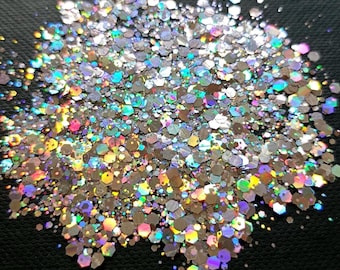 May include: Close-up of a pile of iridescent glitter. The glitter is composed of many small, hexagonal pieces that reflect a rainbow of colors. The glitter is silver and reflects light in a variety of colors, including pink, blue, and green.