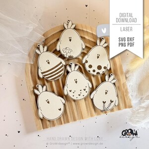 May include: Six light-colored wooden egg-shaped ornaments with laser-engraved chick designs, including patterns of stripes, dots, hearts, and a flower. The text DIGITAL DOWNLOAD LASER SVG DXF PNG PDF is visible on a white banner overlay.