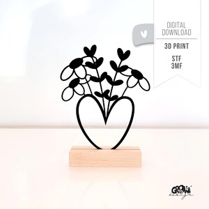 May include: A black metal flower arrangement in a heart-shaped vase, on a wooden base. The flowers have white petals and black centres. The image includes the text "DIGITAL DOWNLOAD", "3D PRINT", "STF 3MF".