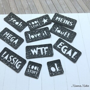 K&ouml;nnte beinhalten: Schwarze und wei&szlig;e rechteckige Aufkleber mit verschiedenen W&ouml;rtern und S&auml;tzen, darunter "yeah", "cool stuff", "love it", "wtf", "meins", "lauft", "egal", "mega", "lassig" und "ok".