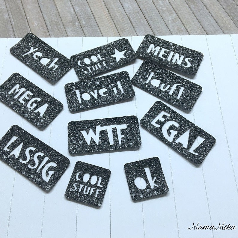 K&ouml;nnte beinhalten: Schwarze und wei&szlig;e rechteckige Aufkleber mit verschiedenen W&ouml;rtern und S&auml;tzen, darunter "yeah", "cool stuff", "love it", "wtf", "meins", "lauft", "egal", "mega", "lassig" und "ok".