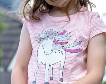 Könnte beinhalten: Ein rosa-weiß gestreiftes T-Shirt mit einem weißen Einhorn-Motiv. Das Einhorn hat eine rosa-blaue Mähne und einen Schwanz sowie eine Blumenkrone mit Perlen.
