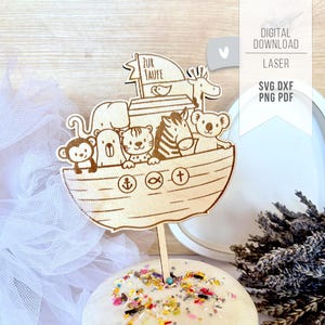 May include: A wooden cake topper featuring Noah's Ark with various animal figures. The ark has the text "ZUR TAUFE" on a sail. The topper is placed on a frosted cake with colorful sprinkles. The design is laser cut.