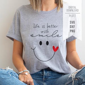 May include: A heather grey t-shirt featuring the black text "life is better with smile" above a black smiley face graphic with a small red heart accent. The image includes text in the upper right corner reading "DIGITAL DOWNLOAD PLOTT SVG DXF PNG".