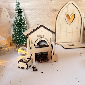 Könnte beinhalten: Miniatur-Holzbäckerei mit dem Text "Wichtel Brot", einem kleinen Baum und einer Feentür. Die Bäckerei hat einen gewölbten Ofen, eine kleine Kiste mit Brot und eine Schaufel. Die Feentür hat ein herzförmiges Fenster und eine Leiter.