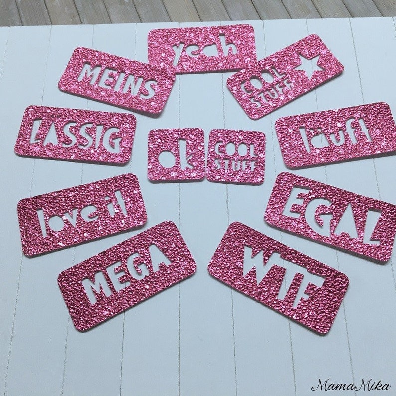 K&ouml;nnte beinhalten: Rosa glitzernde Karton-Ausschnitte mit verschiedenen W&ouml;rtern und Phrasen, darunter "yeah", "cool stuff", "meins", "lassig", "love it", "mega", "wtf", "egal", "lauff", "ok" und "cool stuff".