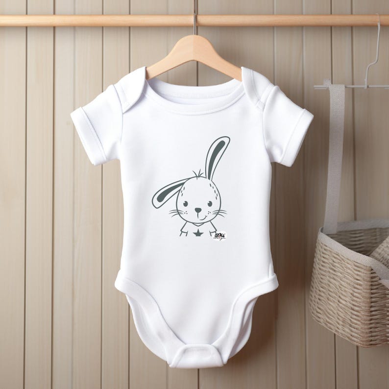 May include: White baby onesie with a gray cartoon bunny wearing a shirt with a star on it.