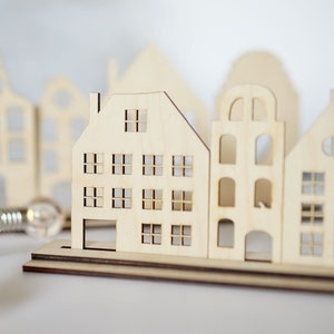 May include: A set of wooden houses with cut-out windows, arranged in a row on a wooden base. The houses are light brown and have a rustic, farmhouse style.