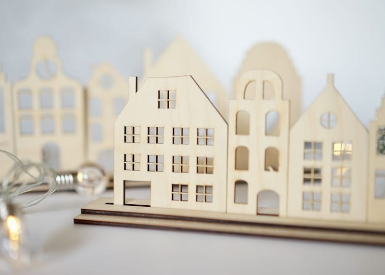 May include: A set of wooden houses with cut-out windows, arranged in a row on a wooden base. The houses are light brown and have a rustic, farmhouse style.