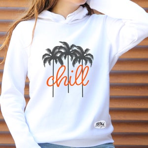 Peut inclure: Sweat-shirt à capuche blanc avec un motif de palmier noir et le mot "chill" en lettres orange.